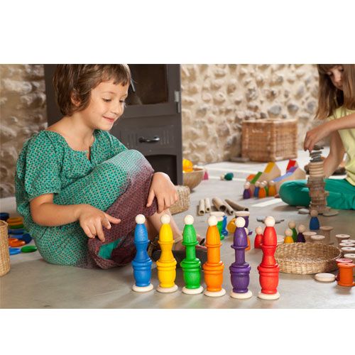 Een kind zit op de grond en speelt met gekleurde houten stapelpoppetjes.