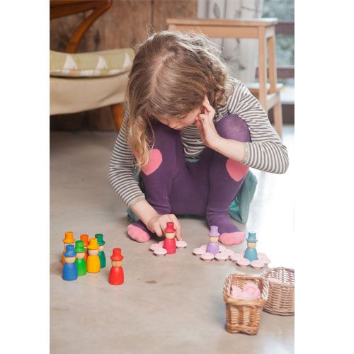 Een kind speelt op de grond met Grapat houten nins poppetjes met hoed, waarvan sommige gestapeld zijn.