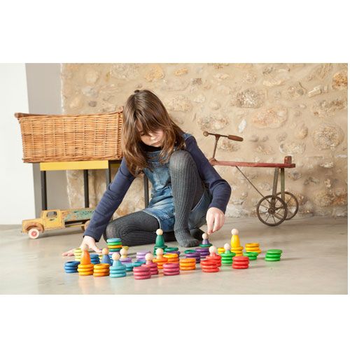 Een meisje speelt op de grond met het Grapat houten sorteer- en stapelspeelgoed, bestaande uit Nins poppetjes, ringen en schijfjes.