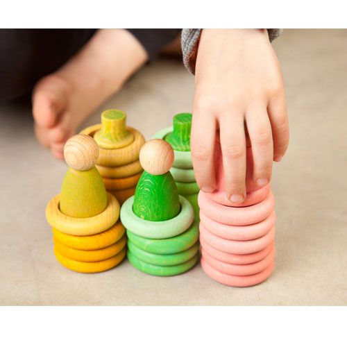 Een kinderhand stapelt roze ringen op een Grapat houten nins® poppetje, onderdeel van het sorteer- en stapelspeelgoed.