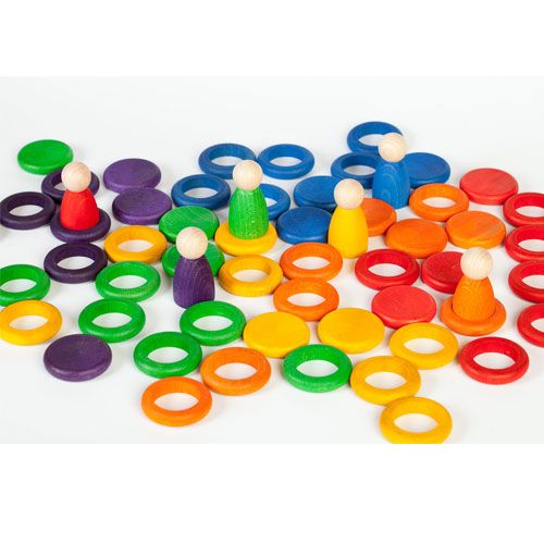 Grapat houten nins® poppetjes, ringen en schijfjes in regenboogkleuren verspreid op een witte ondergrond.