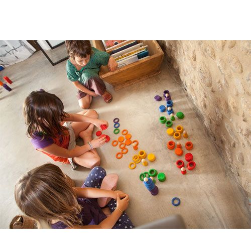 Drie kinderen spelen op de grond met het Grapat houten sorteer- en stapelspeelgoed in regenboogkleuren.