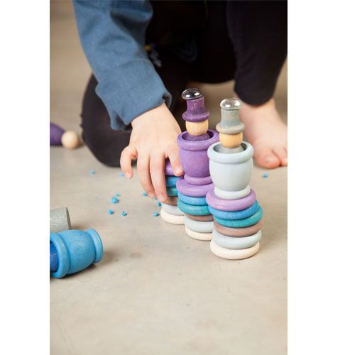 Een kind stapelt Grapat houten Nins poppetjes en ringen in winterkleuren op de vloer.
