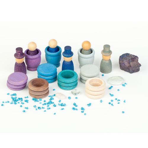 Grapat houten Nins poppetjes, ringen en schijfjes in winterkleuren liggen op een witte ondergrond met kleine blauwe steentjes en een donkere rots.
