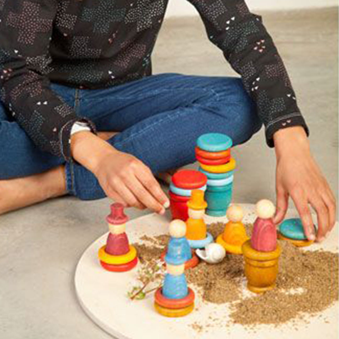 Een kind speelt met Grapat houten nins® poppetjes, ringen en schijfjes op een ronde ondergrond met zand.