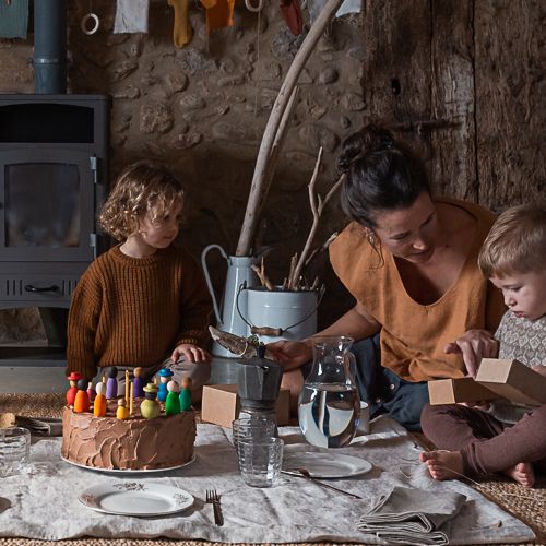 Een vrouw en twee kinderen vieren feest met een chocoladetaart versierd met Grapat houten Nins® poppetjes.