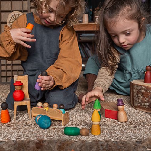 Twee kinderen spelen met Grapat houten Nins® poppetjes en klein houten meubilair op een vloerkleed.