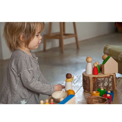 Een kind speelt met Grapat houten Nins poppetjes en andere houten speelgoedfiguren op een houten ondergrond.