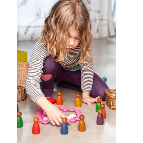 Een kind speelt op de grond met Grapat houten Nins® poppetjes en roze houten speelstukken.