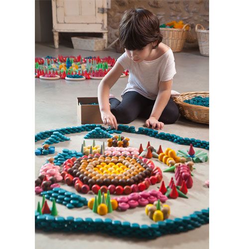 Een kind speelt op de grond met grapat houten bouwspeelgoed, waarmee een grote kleurrijke mandala wordt gevormd.