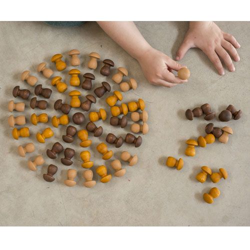 Kinderhanden rangschikken grapat houten paddenstoeltjes in bruin- en oranjetinten op een grijze vloer.