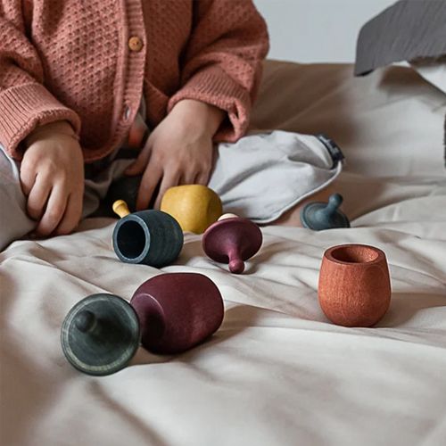 Een kind speelt op een bed met verschillende losse onderdelen van Grapat houten poppetjes in bakjes.