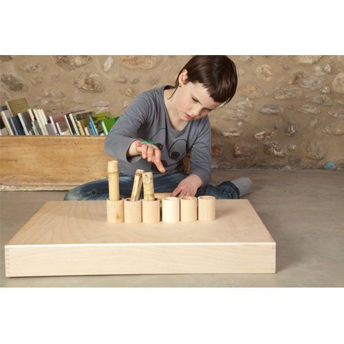 Een kind speelt met de houten potjes en plaatst een stokje in een van de cilinders.