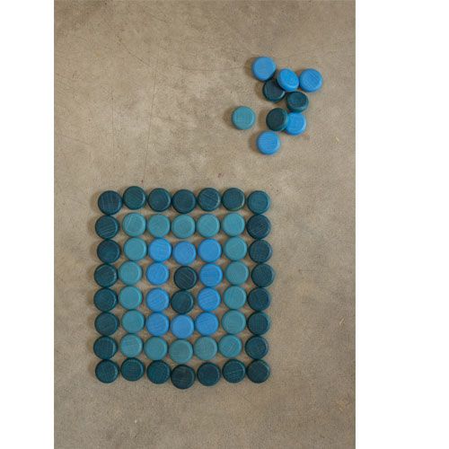 Grapat houten schijfjes in blauwtinten, deels gerangschikt in een vierkant patroon op een betonnen vloer.