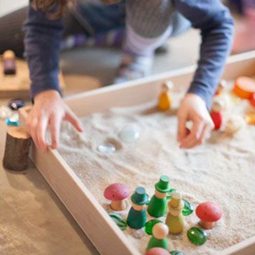 Een kind speelt met zand en houten speelstukken in een Grapat houten speelbak.