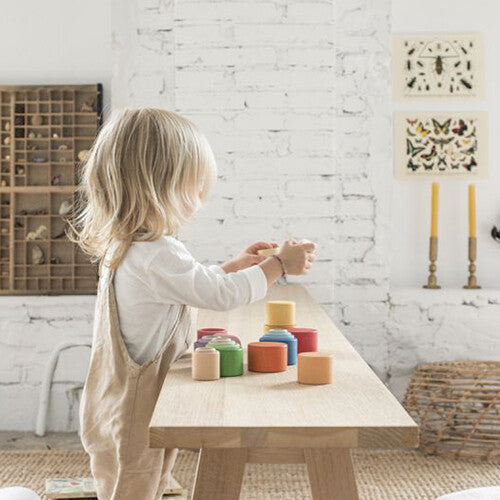 Een kind speelt met Grapat houten stapelbakjes op een houten bankje.