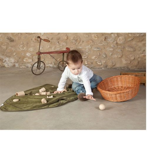 Een baby speelt op een groen kleed met houten vormen en een rieten mand.