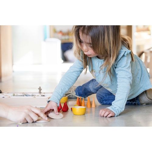 Een kind speelt op de vloer met grapat houten kegels en andere houten speelgoedonderdelen.