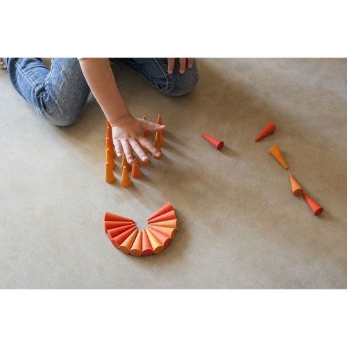 Een kinderhand speelt met grapat oranje houten kegels op de vloer.