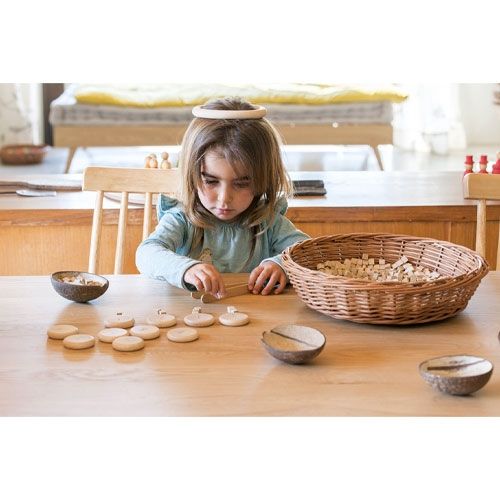 Een jong kind speelt aan een houten tafel met Grapat houten munten met cijfers en kleine houten blokjes.