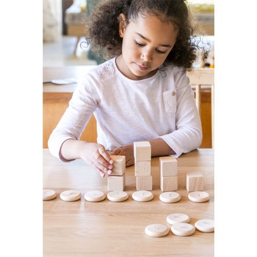 Een kind stapelt houten blokjes op Grapat houten munten met cijfers op een houten tafel.