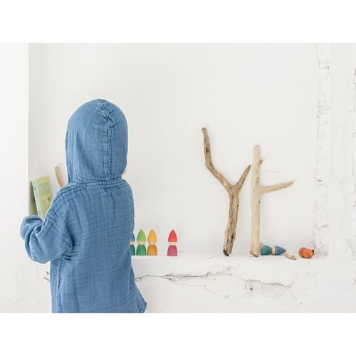 Een kind in een blauwe trui kijkt naar grapat houten kabouter speelgoedfiguurtjes en takken op een plank.