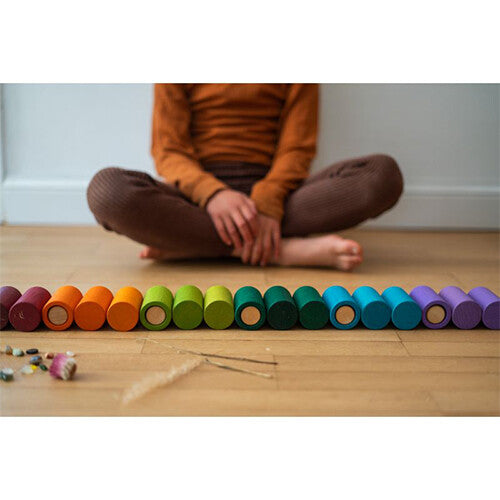 Detail van Grapat houten cilindervormige blokken in regenboogkleuren, liggend op een houten vloer.