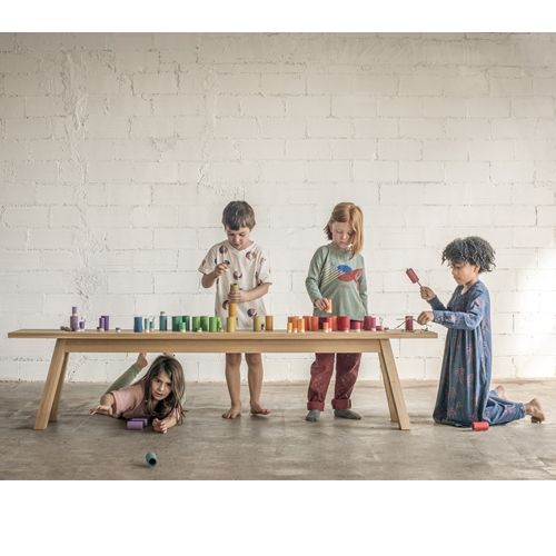 Vier kinderen spelen met de Grapat houten Lola poppetjes aan een lange tafel.