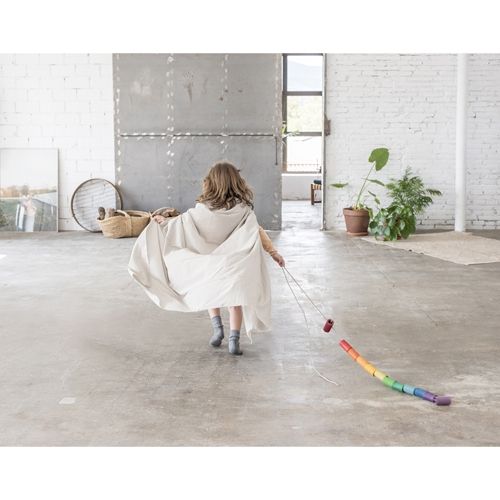 Een kind rent met een cape en trekt een slinger van Grapat houten Lola poppetjes in regenboogkleuren achter zich aan.