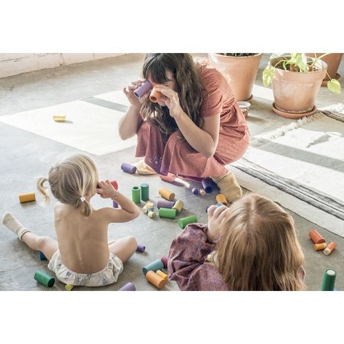 Een volwassene en twee kinderen spelen op de grond met de Grapat houten Lola poppetjes.