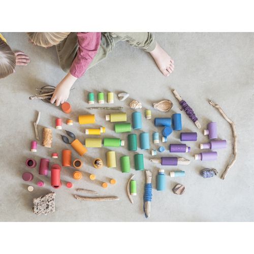 Kinderhanden spelen met Grapat houten Lola poppetjes en natuurlijke materialen op de grond.