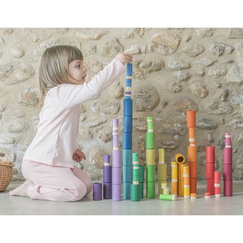 Een kind stapelt Grapat houten Lola poppetjes in regenboogkleuren tot hoge torens.