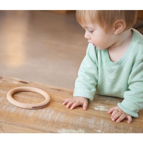 Een baby kijkt naar een Grapat houten ring op een houten tafel.