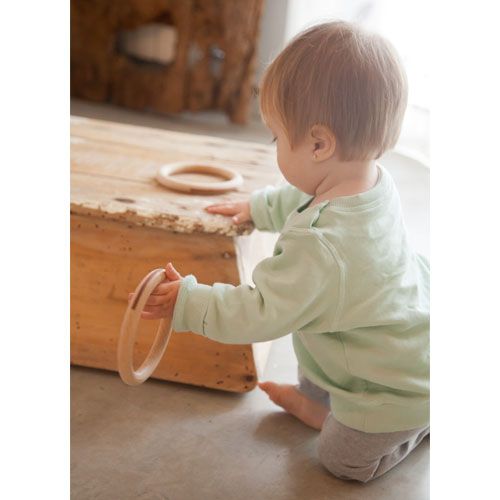 Een baby op de knieën houdt een Grapat houten ring vast.