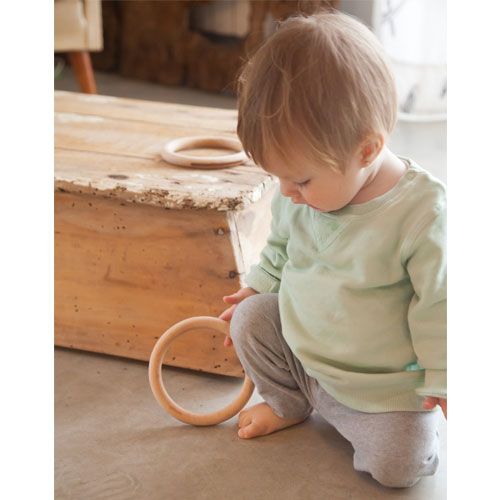 Een baby kijkt naar een Grapat houten ring op de vloer.