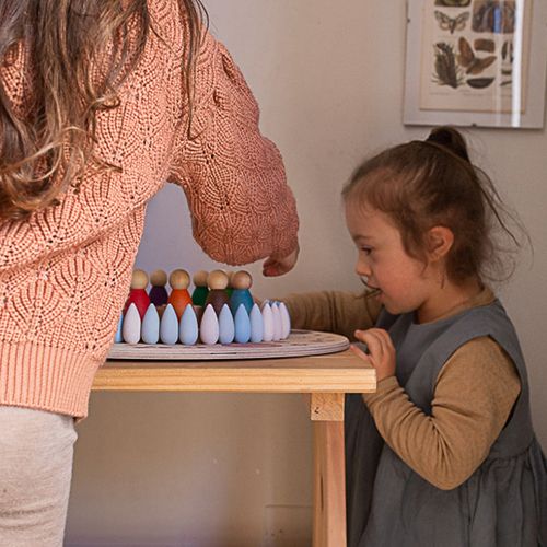 Een kind en volwassene spelen met Grapat houten druppelvormige blokken en peg dolls op een houten tafel.
