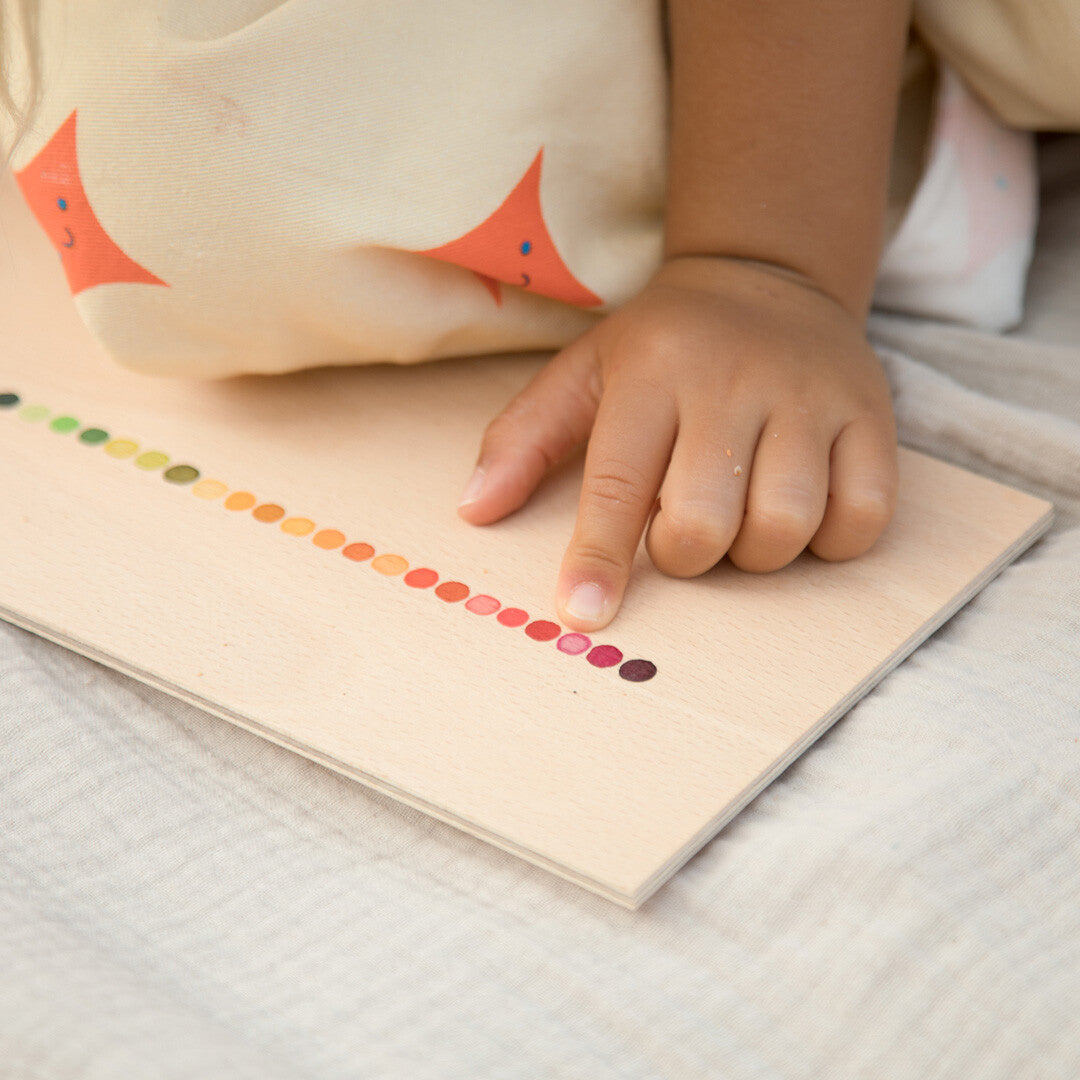 Een kinderhand wijst naar een rode stip op de deksel van de Grapat sorteerbak met regenboogpatroon.