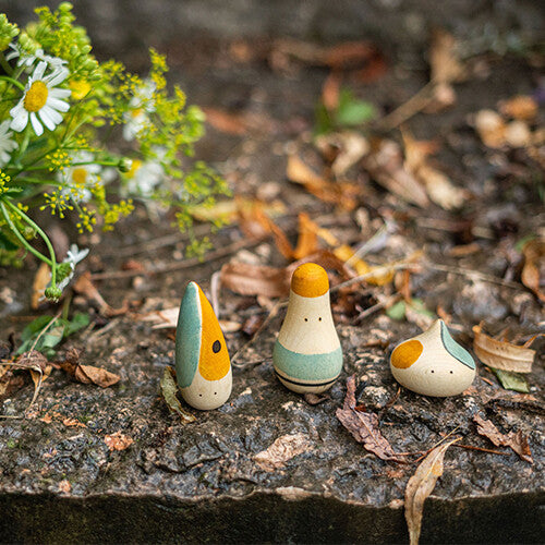 Drie Grapat abstracte houten speelfiguren op een stenen ondergrond met herfstbladeren en bloemen.