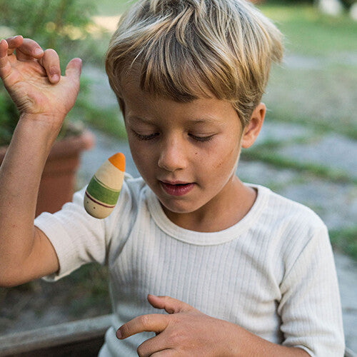 Een jongen houdt een van de grapat houten speelfiguren met oranje en groene strepen in zijn hand.