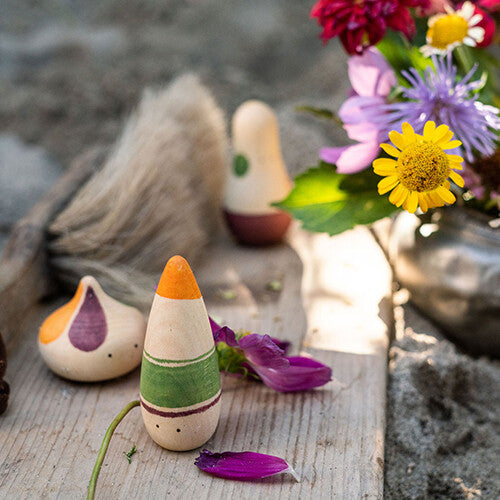 Drie grapat houten speelfiguren liggen op een houten ondergrond met bloemen en bladeren eromheen.