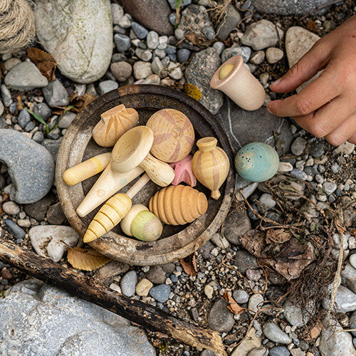 Grapat houten speelfiguren wonders in een kom op een rotsachtige ondergrond, met een kinderhand.