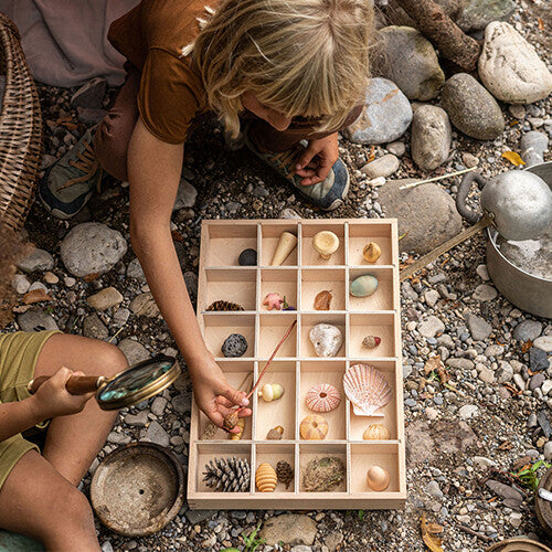 Twee kinderen spelen buiten met een houten sorteerbak gevuld met natuurlijke materialen en Grapat speelfiguren wonders.