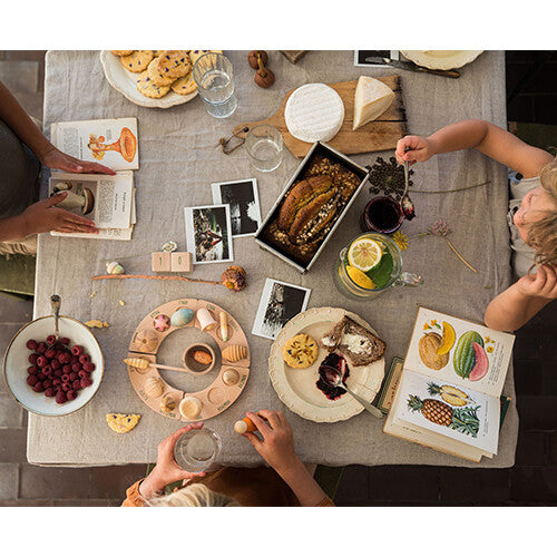 Bovenaanzicht van een tafel met eten, boeken en een Grapat houten jaarring met speelfiguren wonders, met handen die spelen.