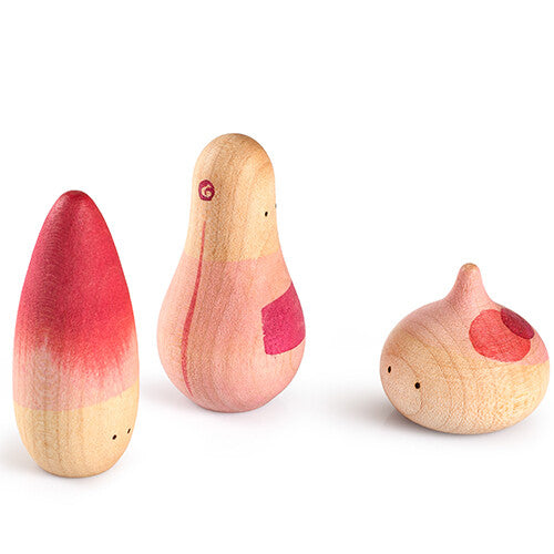 Drie grapat houten speelfiguren in beige met roze en rode accenten, schuin van achteren gefotografeerd.