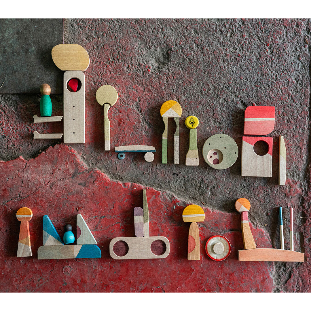 Grapat houten speelset Happy Place met veelkleurige abstracte blokken en figuren, van bovenaf gefotografeerd op een rode ondergrond.