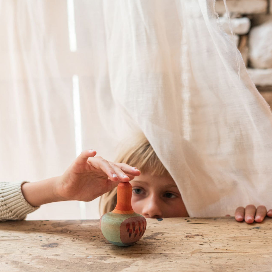 Een kind speelt met een Grapat houten vogel tuimelaar en tol op een houten tafel.