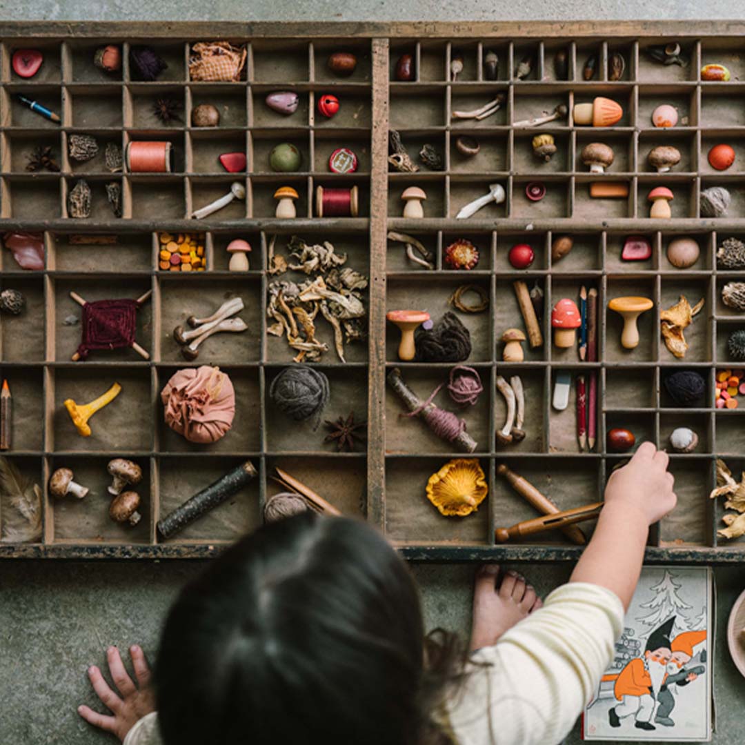 Een kind dat houten paddenstoelen en andere kleine voorwerpen sorteert in een houten vakkenbak.