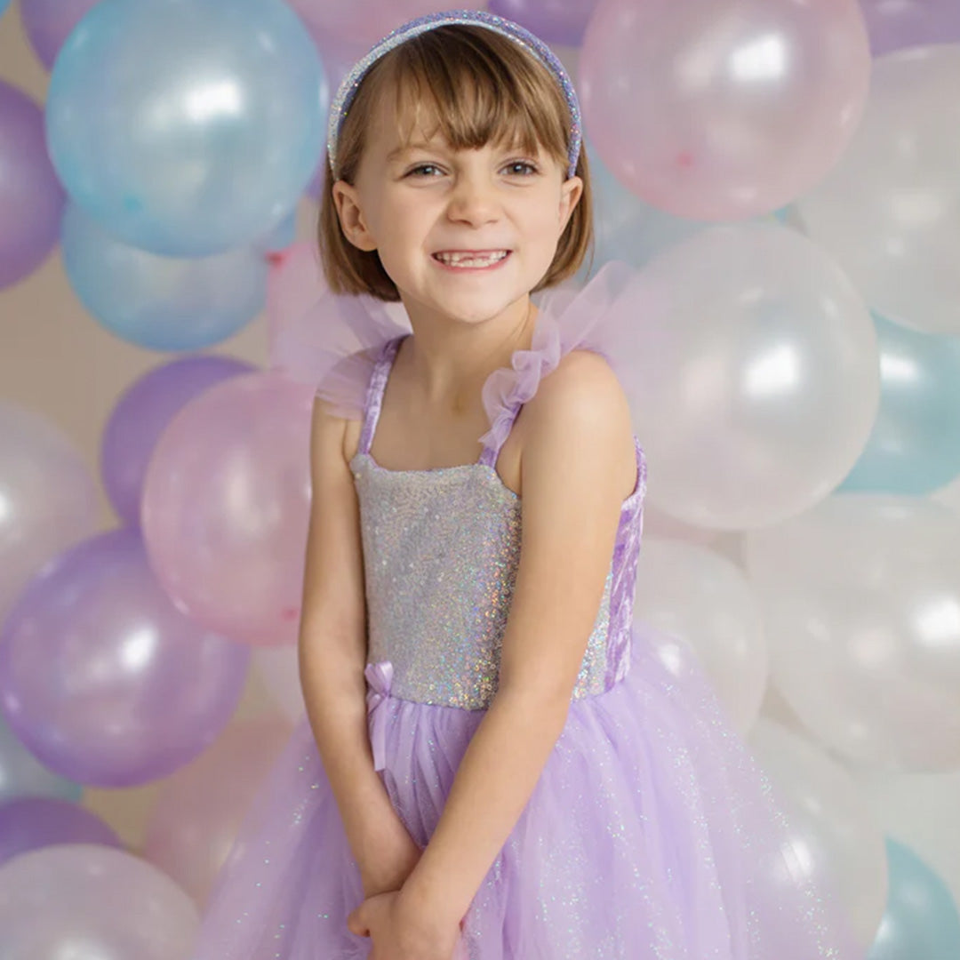 Lachend meisje draagt de paarse prinsessen feestjurk voor een achtergrond van ballonnen.