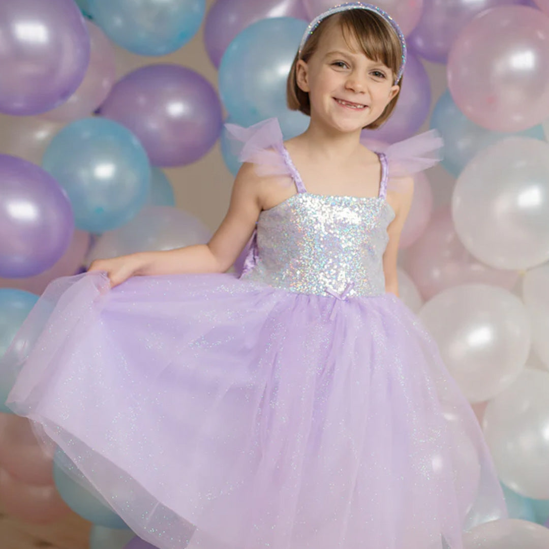 Lachend meisje in de paarse prinsessen feestjurk houdt de tule rok omhoog voor een achtergrond van ballonnen.
