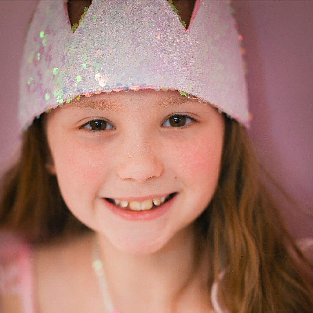 Een meisje met bruin haar lacht terwijl ze de roze pailletten kinderkroon draagt.